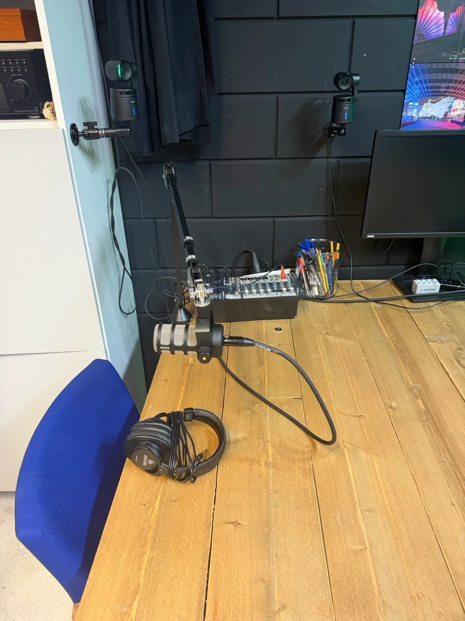 RØDE PodMic en koptelefoon aan de opnametafel, met optionele camera’s aan de wand